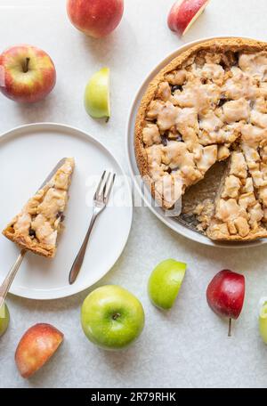 Frisch gebackener Apfelkuchen mit Zimt-, Rosinenfüllung und Zitronenglasur auf weißem Hintergrund mit farbenfroher Apfeldekoration Stockfoto