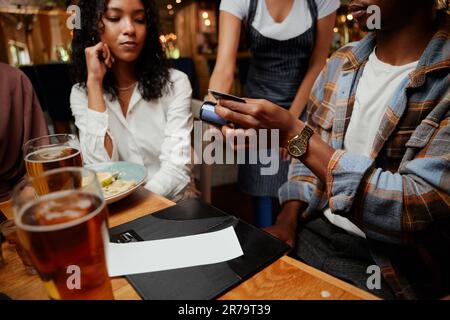 Nahaufnahme multiethnischer Freunde in legerer Kleidung, die Kellnerin für Abendessen und Getränkegarantie an der Bar bezahlt Stockfoto