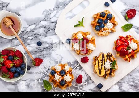 Köstliche belgische Waffeln mit Beere, Obst, Schlagsahne und verschiedenen süßen Belag auf weißem Marmor. Draufsicht. Stockfoto