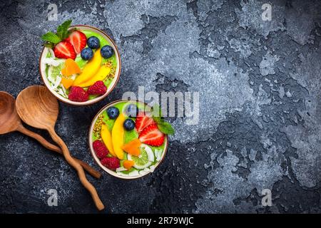 Grüner Smoothie in Schüsseln für gesundes Frühstück. Frischer Bio-Smoothie aus Spinat, Banane, Spirulina, Weizengras und Limette mit Beeren und Obst Stockfoto