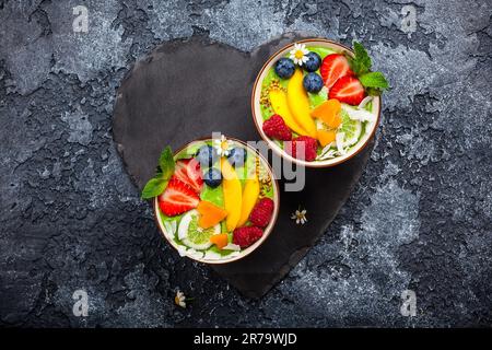 Grüner Smoothie in Schüsseln für gesundes Frühstück. Frischer Bio-Smoothie aus Spinat, Banane, Spirulina, Weizengras und Limette mit Beeren und Obst Stockfoto