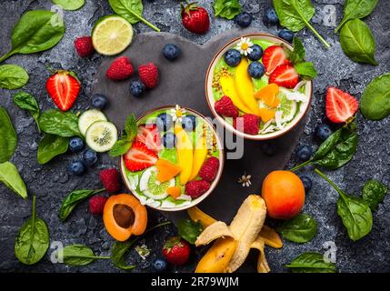 Grüner Smoothie in Schüsseln für gesundes Frühstück. Frischer Bio-Smoothie aus Spinat, Banane, Spirulina, Weizengras und Limette mit Beeren und Obst Stockfoto