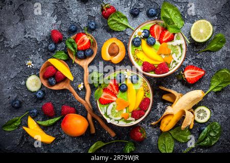 Grüner Smoothie in Schüsseln für gesundes Frühstück. Frischer Bio-Smoothie aus Spinat, Banane, Spirulina, Weizengras und Limette mit Beeren und Obst Stockfoto