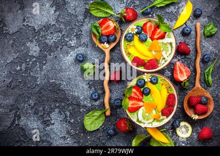 Grüner Smoothie in Schüsseln für gesundes Frühstück. Frischer Bio-Smoothie aus Spinat, Banane, Spirulina, Weizengras und Limette mit Beeren und Obst Stockfoto