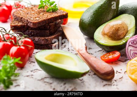 Frische Zutaten für die Zubereitung gesunder vegetarischer Sandwiches mit Schwarzbrot, Avocado und Tomaten. Konzept gesunde Ernährung. Stockfoto