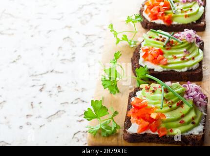 Frische vegetarische Sandwiches auf Schwarzbrot mit Avocado, Tomaten und roten Zwiebeln auf dem Holzbrett. Konzept gesunde Ernährung Stockfoto
