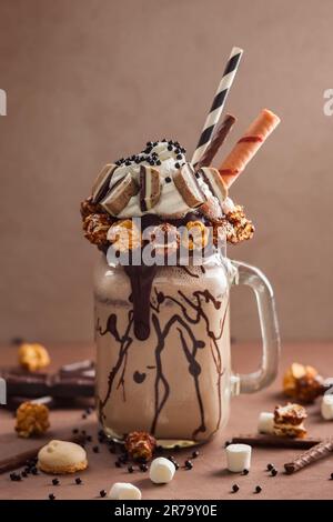 Schokoladenmilchshake mit Eiscreme und mit Schlagsahne, Marshmallow, süßem Popcorn, Keksen, Waffeln, Serviert in einem Glasbecher. „Freak or Crazy“ Stockfoto