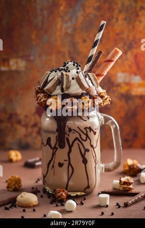 Schokoladenmilchshake mit Eiscreme und mit Schlagsahne, Marshmallow, süßem Popcorn, Keksen, Waffeln, Serviert in einem Glasbecher. „Freak or Crazy“ Stockfoto