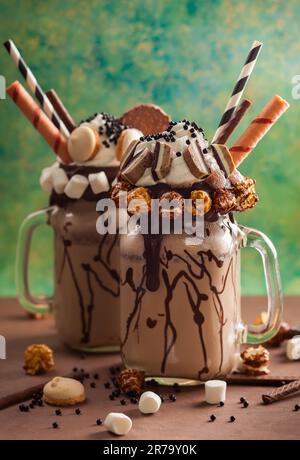 Schokoladenmilchshake mit Eiscreme und mit Schlagsahne, Marshmallow, süßem Popcorn, Keksen, Waffeln, Serviert in einem Glasbecher. „Freak or Crazy“ Stockfoto