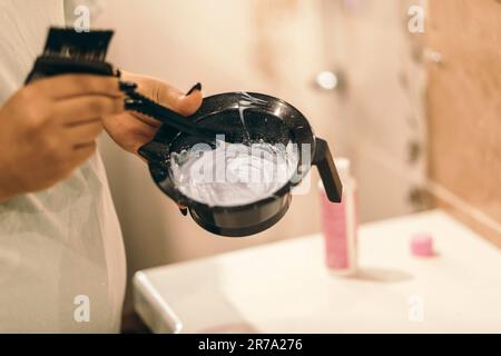 Der Vorbereitungsvorgang für die Haarfärbung zu Hause. Weibliche Hände mit oxidierendem in Kunststoffschüssel mit vorbereitetem Haarfärbemittel. Stockfoto