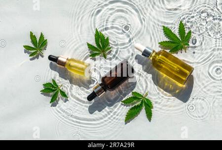 CBD-Ölflaschen, Weißwasser-Hintergrund mit Tropfen, Wellen und Blättern aus Hanf, Marihuana Stockfoto