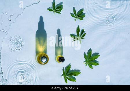 CBD-Ölflaschen, blauer Wasserhintergrund mit Tropfen, Wellen und Blättern aus Hanf, Marihuana Stockfoto