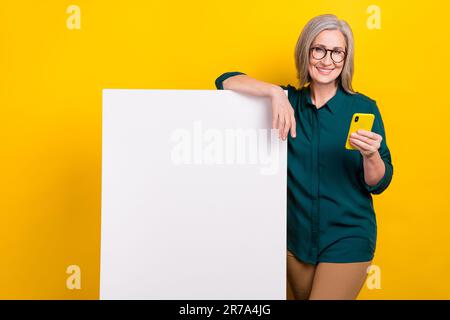 Foto eines positiven eleganten Lady Hold Smartphones mit leerem, isoliertem Space-Banner auf gelbem Hintergrund Stockfoto