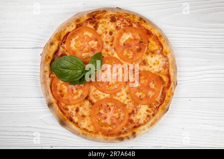 Eine leckere kleine Pizza mit einer dünnen Kruste, garniert mit frischen Tomatenscheiben, Spinat und geschmolzenem Käse Stockfoto