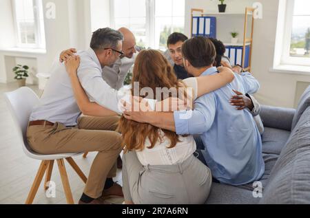 Ein Team aus verschiedenen Geschäftsleuten und Freunden, die im Kreis sitzen und sich umarmen Stockfoto