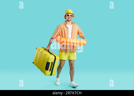 Ein fröhlicher junger Mann mit Koffer und aufblasbarem Kreis fährt in den Sommerurlaub in ein Strandresort. Stockfoto