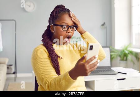 Eine wunderschöne afrikanische Frau sieht vor Schrecken auf das Telefon. Stockfoto