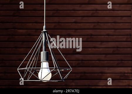 Nahaufnahme einer modernen Pendelleuchte, die auf einem hölzernen Wandhintergrund hängt, Kopierbereich Stockfoto