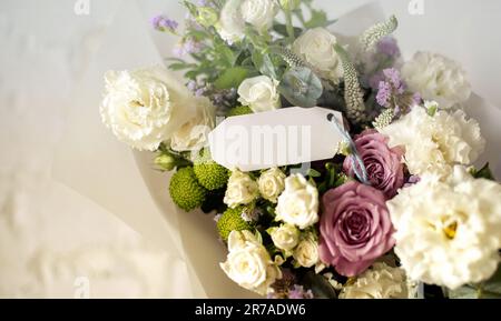 Ein lebhafter Blumenstrauß, bestehend aus rosa Rosen, gelben Tulpen und lila Pissos, angeordnet in einer durchsichtigen Vase und mit einem verbunden Stockfoto