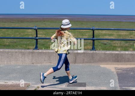 Junge Frau, die in der Sommerhitzewelle in Southport, Merseyside läuft. UK Weather 14. Juni 2023. Stadtratsvernachlässigung im Küstenresort, mit Strandbarrieren, einem Pier, der geschlossen ist, und einer alles andere als verlassenen Promenade und Strandbereich. Stockfoto