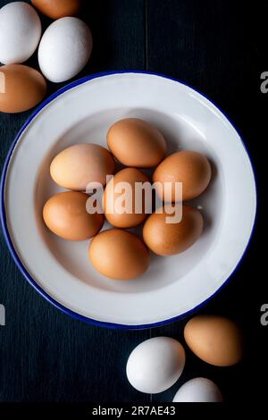 Frische braune und weiße Eier in einer Emaillschüssel auf rustikalem Holzhintergrund mit Kopierbereich. Draufsicht. Natürliche gesunde Bio-Lebensmittel, Kochkonzept. Stockfoto