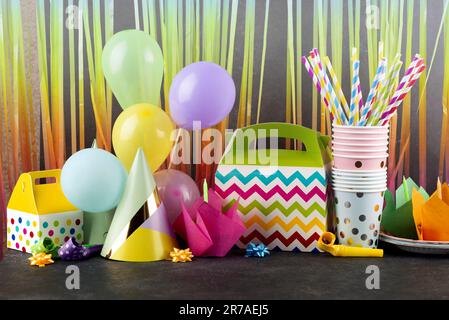 Eine große Auswahl an pulsierenden Partyartikeln, darunter Plastikbecher, Papierhalme, Ballons und Papierhüte auf einer Holzfläche Stockfoto