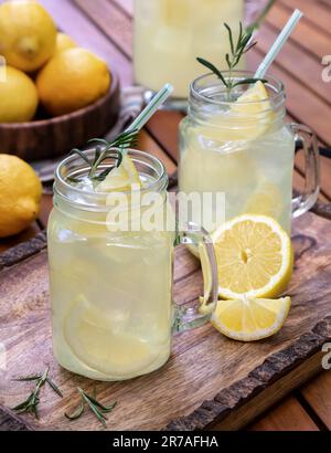 Limonade in zwei Glas jaes mit Zitronenscheiben, Rosmarin und Eis auf einem Holztablett Stockfoto