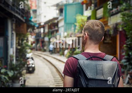 Ein Mann mit Rucksack, der durch die schmale Train Street läuft. Eisenbahnstrecke zwischen Wohngebäuden in Hanoi Vietnam. Stockfoto