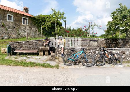 Mutter und Sohn, Touristen, Radfahrer auf einer Radtour durch die Istrien-Halbinsel in Slowenien, entspannen auf einer Steinmauer eines Brunnens in abitanti, slowenien Stockfoto