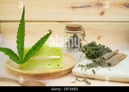 Cannabisgelenke vor dem Rollen und Kuchen mit Cannabisknospen in einem durchsichtigen Glasgefäß, der auf dem Sacktuch liegt Stockfoto