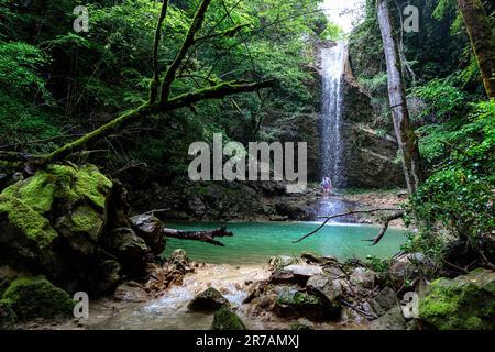 Touristen an einem wunderschönen und malerischen Butori-Wasserfall umgeben von üppiger Vegetation mit türkisfarbenem See am Grund des Abgrunds, Kroatien Stockfoto