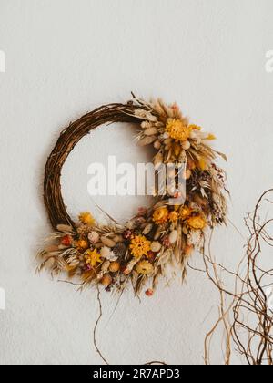 Der natürliche, wunderschöne Kranz verschiedener getrockneter Blumen und Pflanzen hängt auf dem weißen Wandhintergrund. Natürliche Inneneinrichtung. Vorderansicht Stockfoto