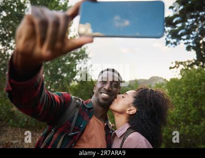 Ein junges, multiethnisches Paar lächelt und macht ein Selfie während einer Wanderung Stockfoto
