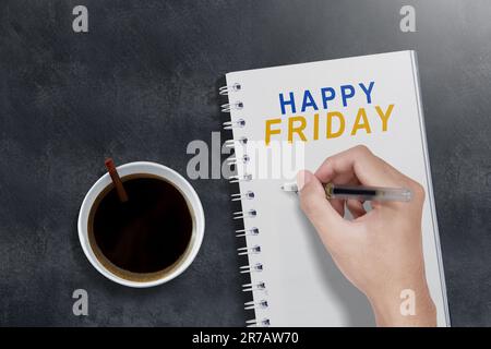 Kaffeetasse mit menschlicher Hand, die Text zum Happy Friday auf ein Notizbuch schreibt. Happy Friday Concept Stockfoto