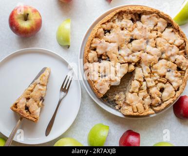 Frisch gebackener Apfelkuchen mit Zimt-, Rosinenfüllung und Zitronenglasur auf weißem Hintergrund mit farbenfroher Apfeldekoration Stockfoto