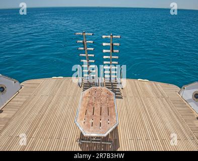 Metall-Stahlleitern auf dem hinteren Teakholz-Deck einer großen Luxusmotoryacht, die auf einem tropischen Ozean segelt Stockfoto