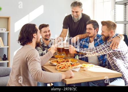 Eine Gruppe glücklicher Männer, die am Tisch sitzen, Bier trinken, Pizza essen und Spaß haben Stockfoto