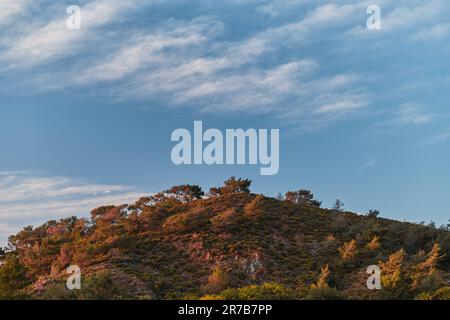 Malerische Landschaft eines Hügels vor einem Himmel aus Federwolken im roten rosa Sonnenuntergang an der ägäischen Küste der Türkei, Landschafts- oder Bildschirmschoner-Idee Stockfoto