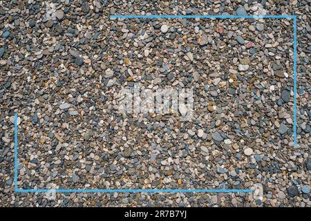 Blauer Rahmen auf dem Hintergrund der Textur runder Kieselsteine. Kieselsteinstrand, dunkle runde Kieselsteine und graue trockene Kieselsteine, Werbe- oder Posteridee Stockfoto