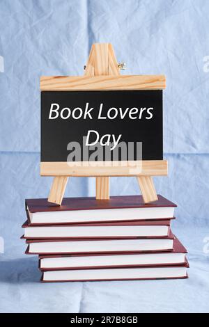 Der Tag der Buchliebhaber steht auf schwarzem Brett auf einem Stapel Bücher auf blauem Hintergrund. Buchurlaub, Bildungskonzept. Stockfoto