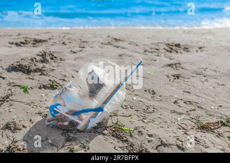 Ein Haufen Abfall in einer Packung liegt auf dem Strandsand gegen das Meer. Das Konzept der Verschmutzung und der Umwelt. Stockfoto