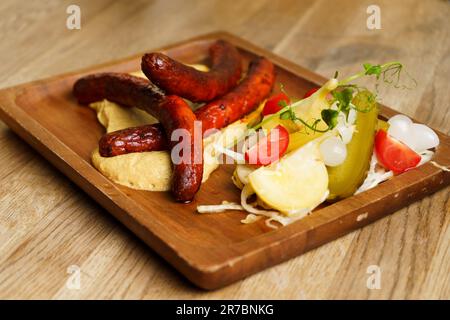 Grillwurst mit Apfelsenf und Gurken auf einem Holzteller. Stockfoto