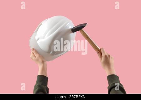 Weibliche Hände mit Schutzhelm und Hammer auf pinkfarbenem Hintergrund Stockfoto