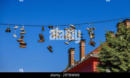 Street Art Installation vieler Paar Schuhe und Turnschuhe, die an ihren Schnürsenkeln hängen, von einem Telegrafendraht auf den Dächern von metelkova ljubljiana Stockfoto