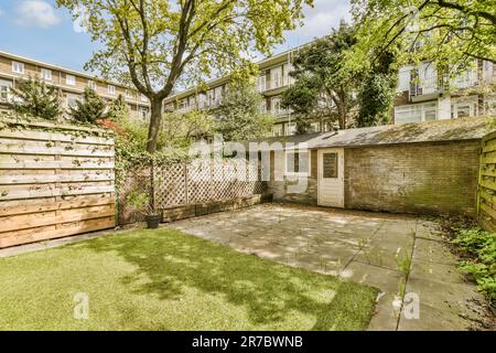 Ein Hinterhof mit Gras, Bäumen und eingezäunt in die Rückseite eines Apartmentgebäudes an einem sonnigen Tag Stockfoto