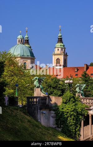 Die grünen Kuppeln der kathedrale von ljubljana über der grünen Drachenstatue auf der berühmten Drachenbrücke von ljubljana Stockfoto