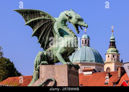 Die grüne Drachenstatue auf der Drachenbrücke von ljubljana, die das Kreuz auf der grünen Kuppel der Kathedrale von ljubljana verschlingen wird Stockfoto