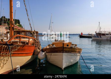 Hölzerne Boote, die auf einem ruhigen Meer im Hafen von Piran festgemacht sind, während eine Yacht an den grünen und roten Leuchttürmen des Hafens vorbeisegelt Stockfoto