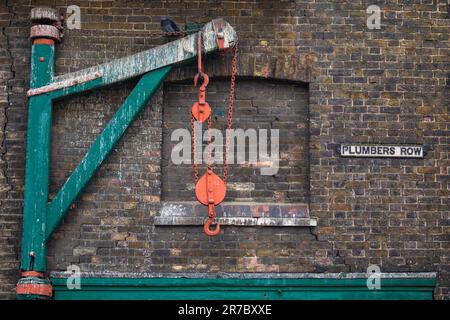Blick auf eine alte Hebebühne und das Straßenschild für Plumbers Row, gleich neben der Whitechapel Road in Tower Hamlets, London, Großbritannien. Stockfoto