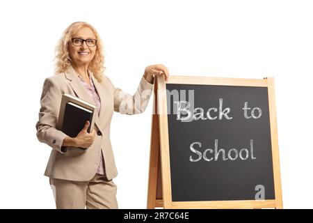 Lehrerin mit Büchern, die sich an eine Tafel lehnt, mit Text zurück zur Schule, isoliert auf weißem Hintergrund Stockfoto